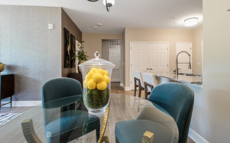 a dining room table with chairs and a glass vase with fruit in it